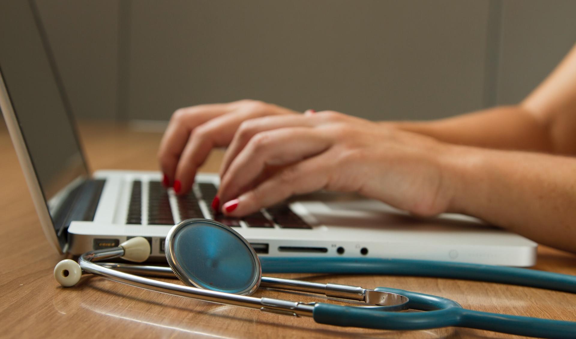 person sitting while using laptop computer and green stethoscope near